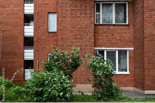 Facade of a brick building with windows and balconies trees grow nearby, city, town © Hleb