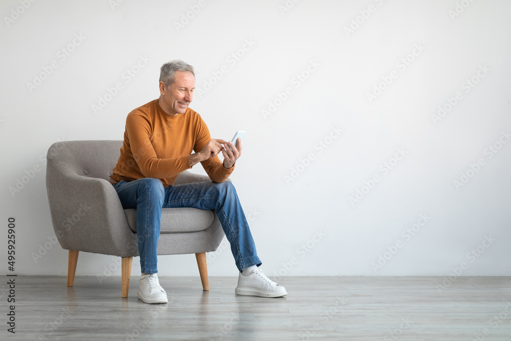 Portrait of mature man using smartphone sitting on armchair Portrait of mature man using smartphone sitting on armchair