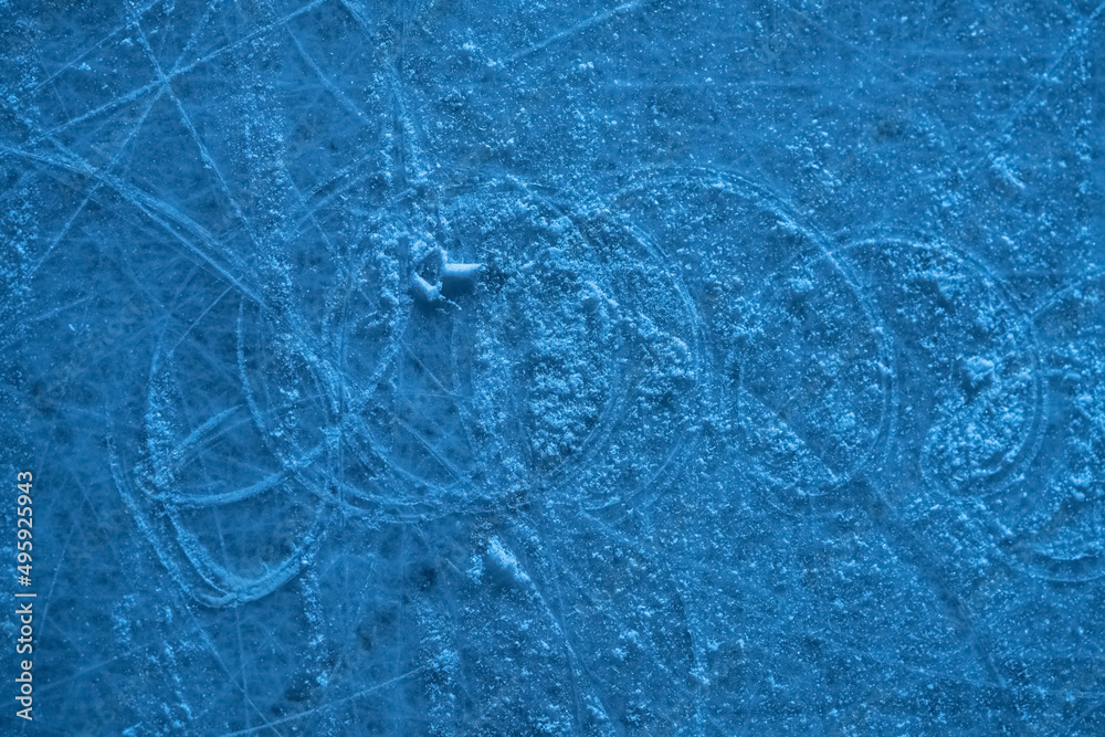 Naklejka premium Ice surface in sports arena for figure skating or hockey. Ice background and ice texture is cut with pattern and scratches from skates. Detail of textured ice with snow in blue light. Close up.