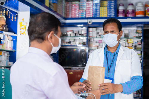 customer purchasing medicines from pharmacist while both in medical face mask at retail store during covid-19 coronavirus pandemic - concept of healcare, medical and safety measures. photo