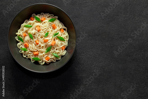 Noodles instant cooked with vegetables carrot and green onion dark bowl, on dark background, top view, space to copy text.