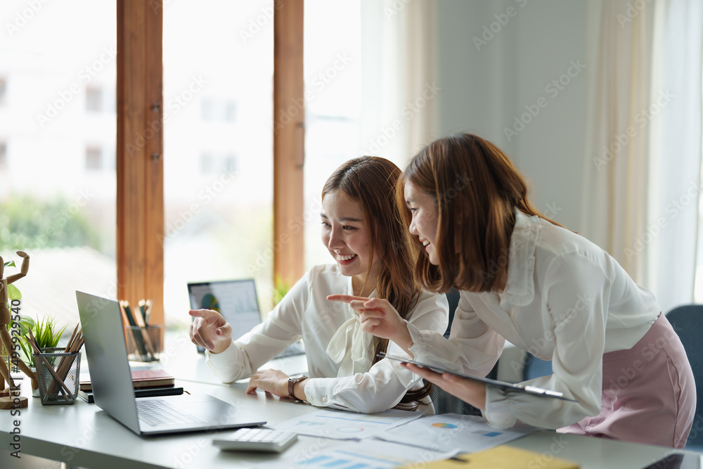 Two colleagues or students, asian girl are using a laptop while sitting at workplace discussing about job or education Two colleagues or students, asian girl are using a laptop while sitting at workplace discussing about job or education
