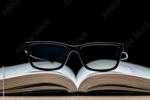 Eyeglasses lie on an open book on a black background. Reading Glasses. Classic black frame glasses.