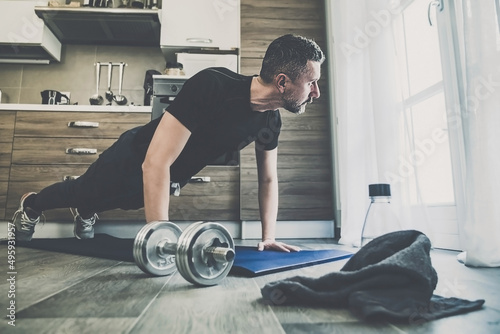 Determined sporty young man working out and trains at home. Fit boy doing push-ups exercises on the mat. Strong boy do gymnastics in the living room. Wellness, health, sport, gym, training concept photo