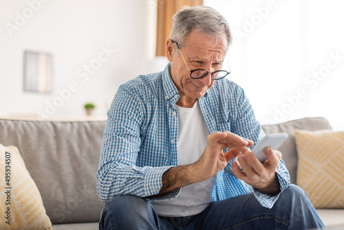 Mature man squinting using cell phone, looking at screen photo