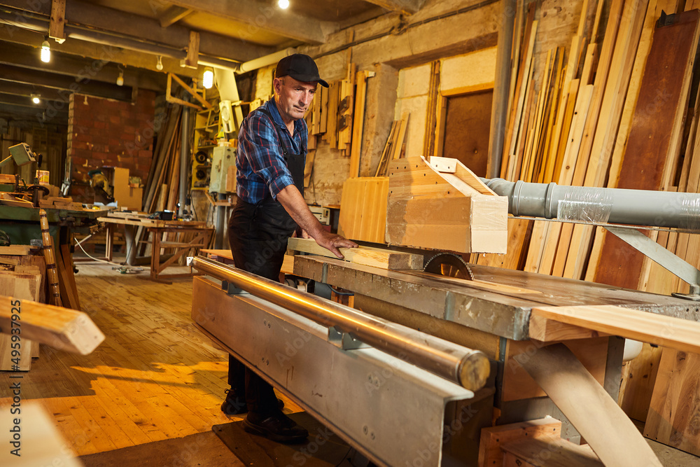 Wood cutting table with electric circular saw. Senior Professional carpenter in uniform cutting wooden board at sawmill carpentry manufacturing . Sawing machine Wood cutting table with electric circular saw. Senior Professional carpenter in uniform cutting wooden board at sawmill carpentry manufacturing . Sawing machine