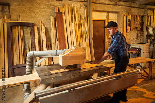 Wood cutting table with electric circular saw. Senior Professional carpenter in uniform cutting wooden board at sawmill carpentry manufacturing . Sawing machine