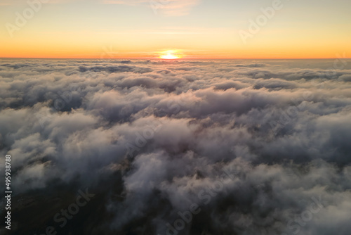 Aerial view from above at high altitude of dense puffy cumulus clouds flying in evening. Amazing sunset from airplane window point of view © bilanol