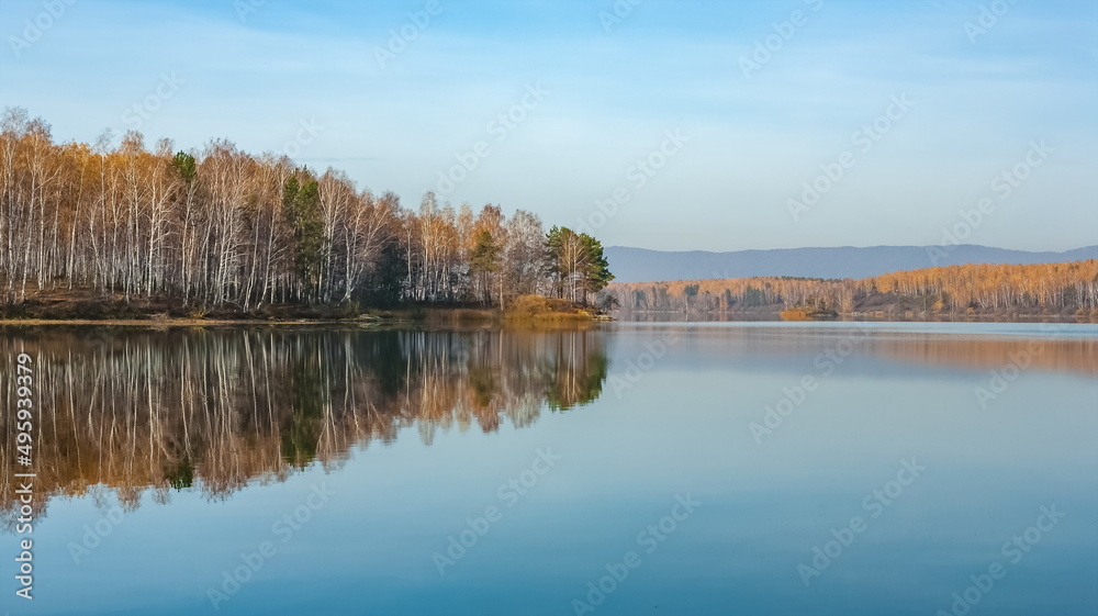 Autumn landscape on the lake with trees, mountains and sky with reflection in the water