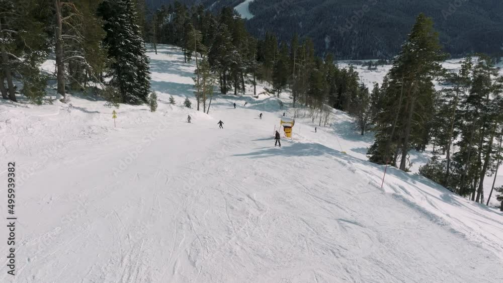 Aerial view of a ski resort with people snowboarding and skiing from a hill. Video footage. Flight over ski or snowboard track on white snow surrounded by thick forest Aerial view of a ski resort with people snowboarding and skiing from a hill. Video footage. Flight over ski or snowboard track on white snow surrounded by thick forest