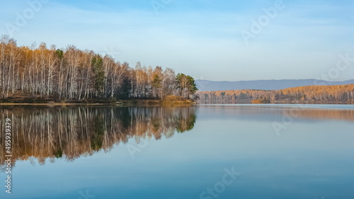 Autumn landscape on the lake with trees, mountains and sky with reflection in the water
