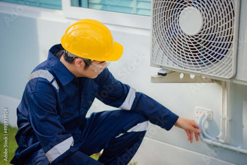 Male technician checking a cooling pipeline of the air conditioner outdoors.