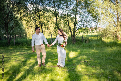 Happy young people in wedding attire walk in the meadow and look at each other