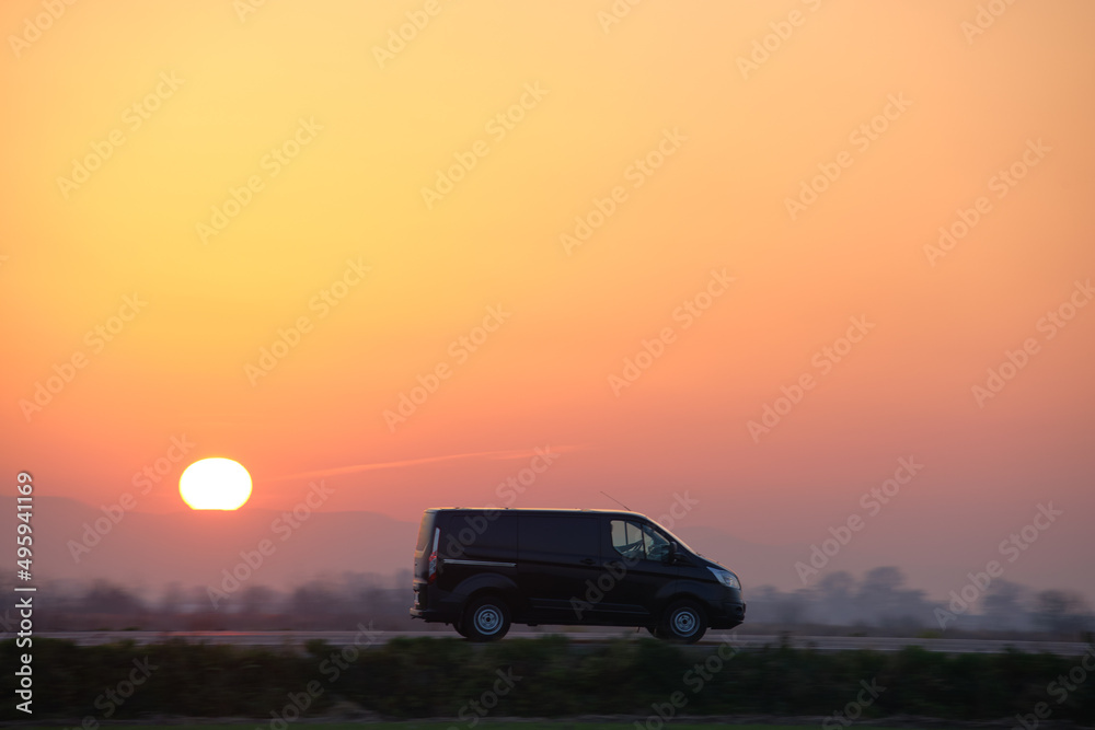 Passenger van driving fast on intercity road at sunset. Highway traffic in evening