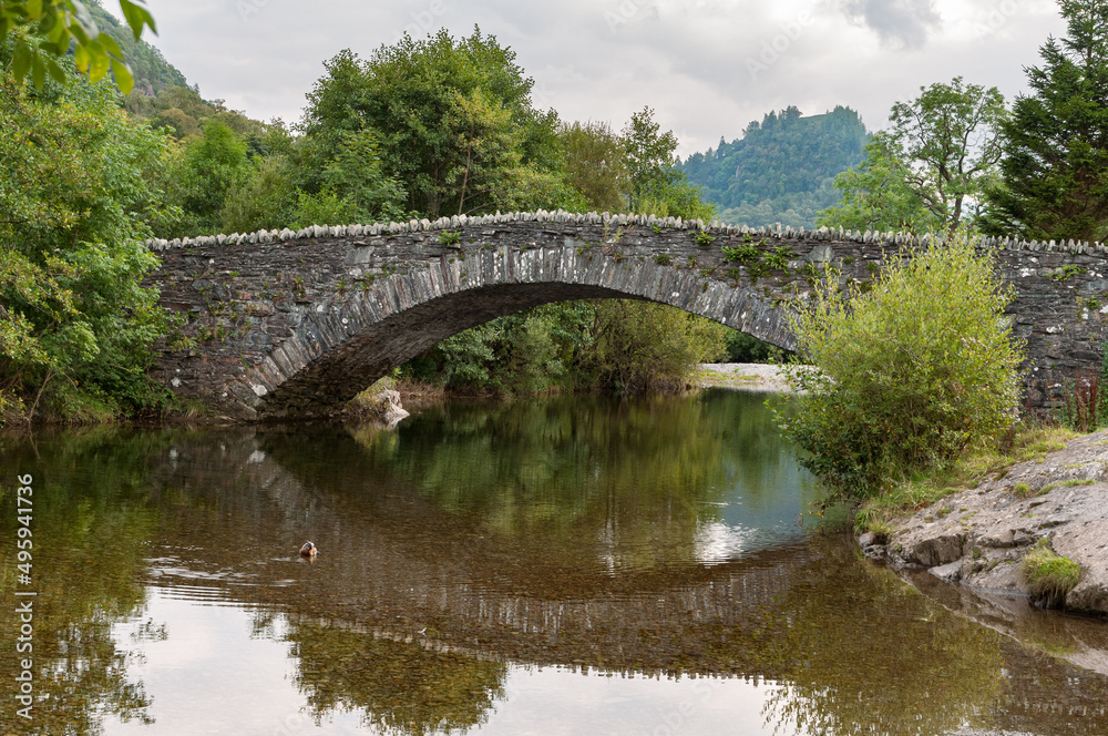 The arched packhorse bridge across the river Derwent in Grange in Borrowdale in the English Lake District with Castle Crag in the background.