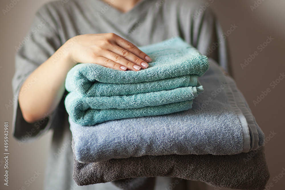 home laundry, female hand holding stack of clean bath towels colorful cotton terry textile background close up, selective focus home laundry, female hand holding stack of clean bath towels colorful cotton terry textile background close up, selective focus