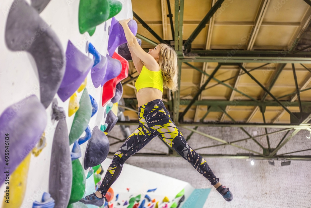 Sportswomen-climbers climbing a steep cliff, climbing an artificial wall indoors. The concept of extreme sports and bouldering.
