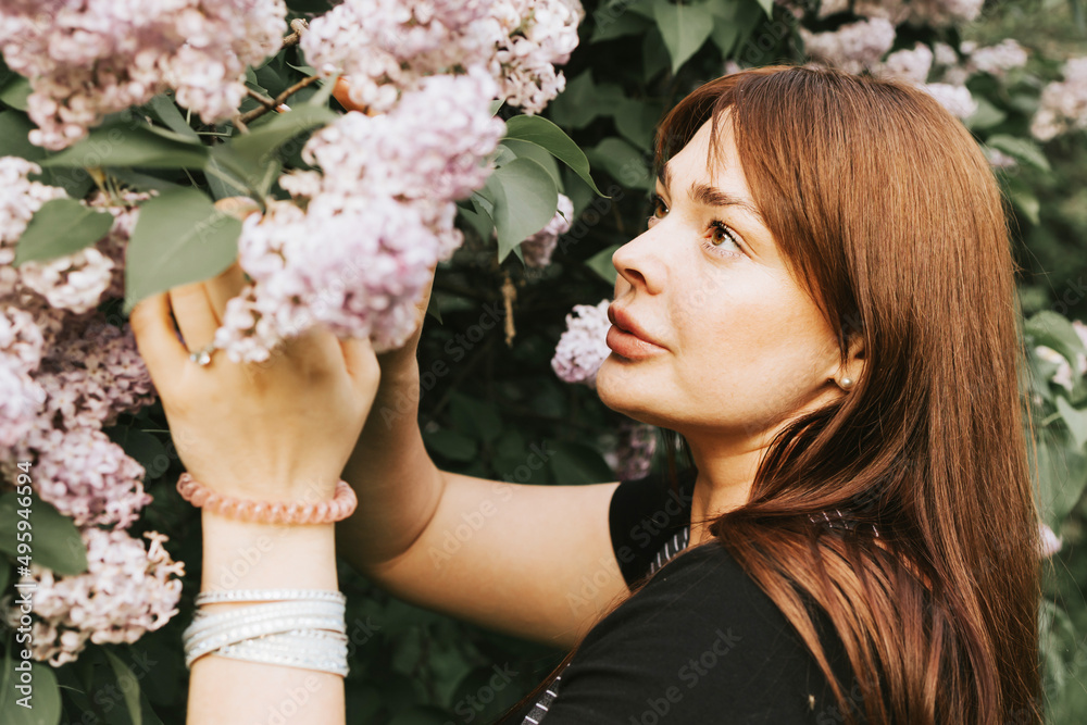 Obraz premium young woman plus size model stands in park next to blooming lilac tree, concept of spring