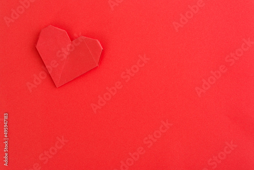 Red origami heart on red background