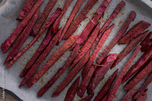 Sliced raw purple sweet potato wedges with spices and oil on parchment paper on a baking sheet