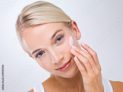 For luxuriously soft skin.... A beautiful young woman applying moisturiser to her face.