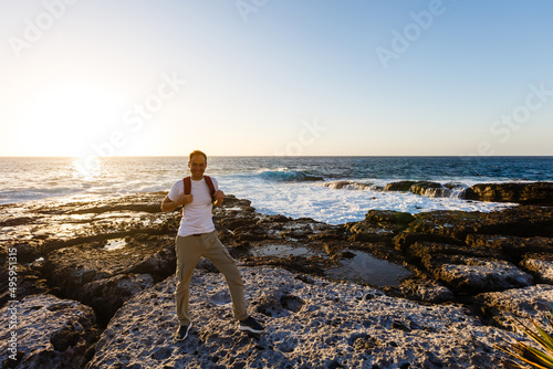 young bright attractive man standing on the ocean and controlling the situation on the beach. Ocean waves and blue sky background
