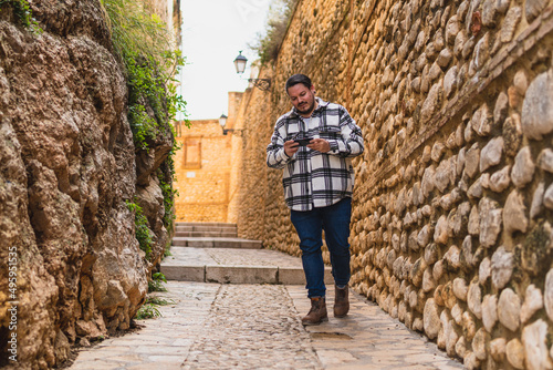 Chico con camisa cuadros blanca posando y tomándose fotos en callejón de piedra en pueblo blanco andaluz