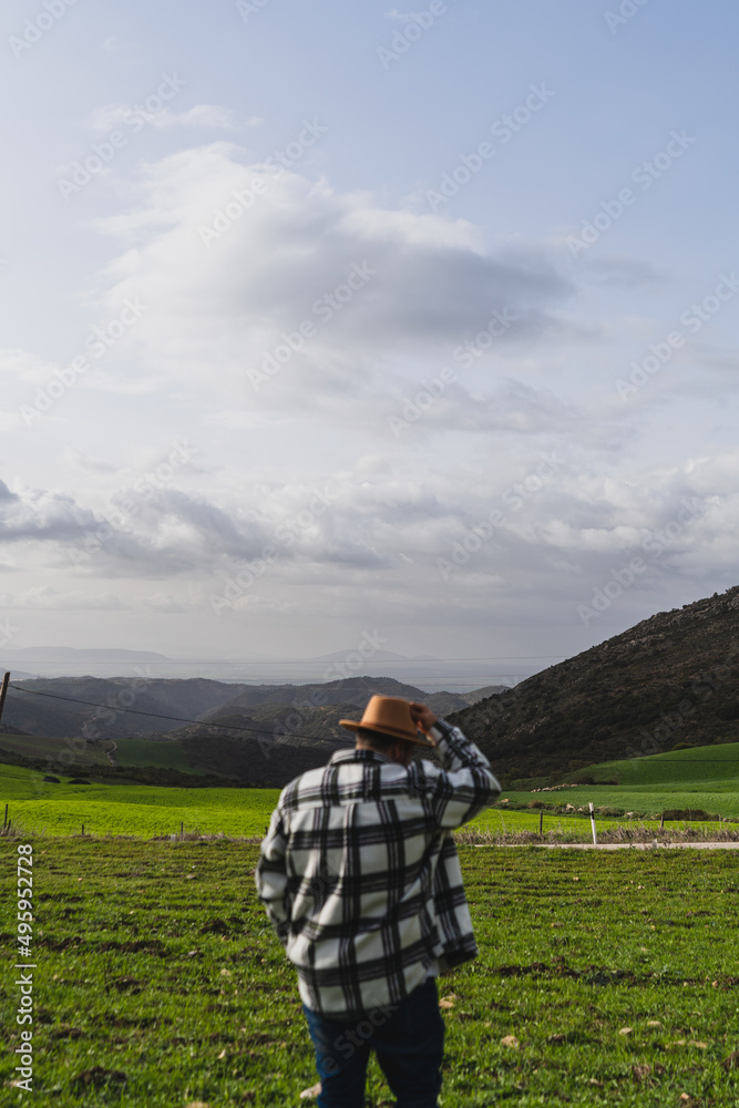 Chico grande con camisa y sombrero frente a paisaje montañoso levantando los brazos y agarrando sombrero en señal de libertad