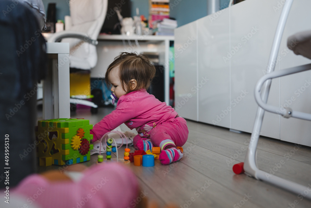One small caucasian baby girl ten months old playing alone at home copy space using bricks and toys wearing pink on the floor in day