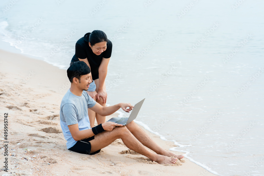 Young Asians sit on a laptop video chatting on a laptop, in a chair by the sea, comfortably, having fun chatting.