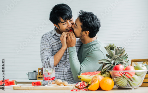 Gay LGBT sweet Asian couple wearing pajamas  smiling  bite  eating piece of watermelon together with happiness   love while having breakfast in kitchen at home in the morning. Lifestyle Concept.