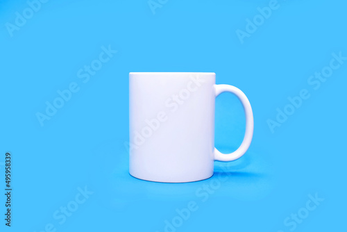 White mug on a blue background in the center. A white cup with any drink on an empty uniform blue background. Cafe or snack concept. White mug with the possibility of advertising or logo