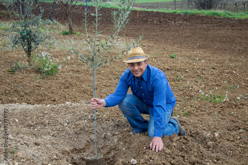 Smiling farmer wearing straw hat while planting an olive tree in a field