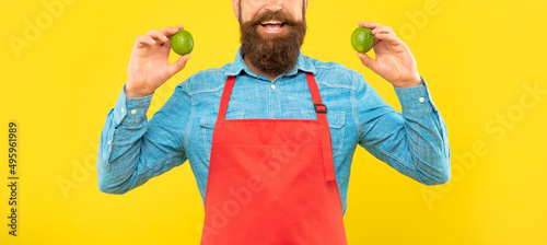 Canvas Print Happy man crop view in red apron holding fresh limes citrus fruits yellow backgr