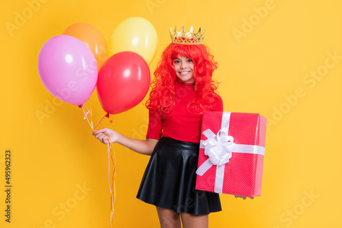glad child in crown with present box and party balloon on yellow background