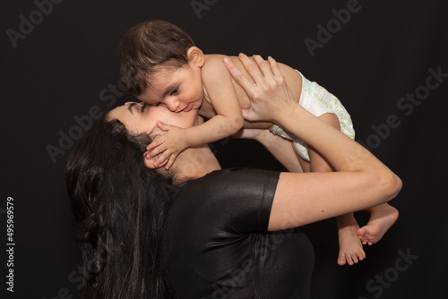 A young mother holds her little son over her head and kisses him. Isolated portrait on black background. © natashaskaya