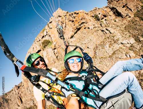 Happy tourist doing paragliding sport activity in outdoor leisure active lifestyle. Cheerful adult woman doing selfie picture flying on a paraglyde in summer holiday vacation. Freedom joyful people