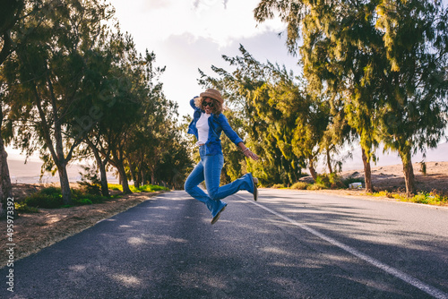 Young adult woman jumping happy in the middle of long straight asphalt road. Concept of travel people and freedom happiness emotions. Casual female have fun and enjoy road trip vacation photo