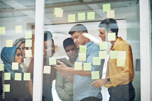 Innovation starts here. Shot of a group of businesspeople using a digital tablet while brainstorming with notes on a glass wall in an office.