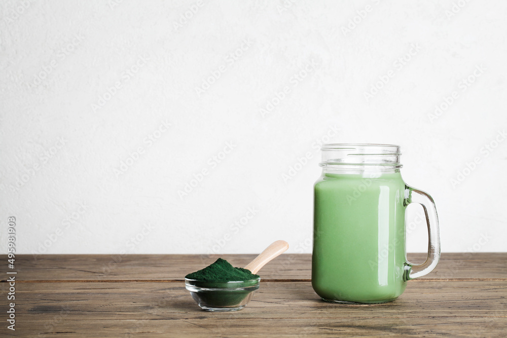 fresh green smoothie in glass bottle and spirulina powder with spoon on wooden background. useful habits, self care and healthy lifestyle. copy space fresh green smoothie in glass bottle and spirulina powder with spoon on wooden background. useful habits, self care and healthy lifestyle. copy space