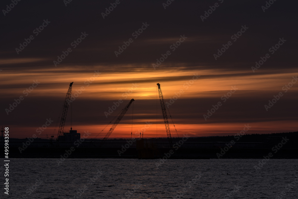 SUNRISE IN COAST - Cranes at the construction site in the sea port 
