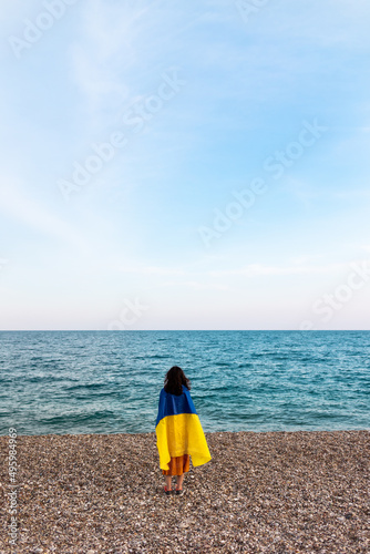 A girl stands by the sea with a Ukrainian flag