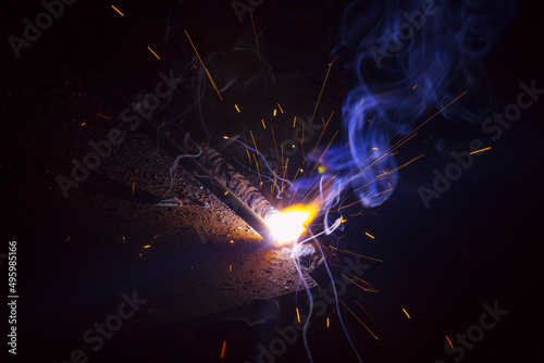 Arc welding. Welding of two sheets of metal by electrode in inert gases. Type MMA. A bright flash of light and a sheaf of sparks in a cloud of smoke. Miniature Universe. Free space for inscriptions.