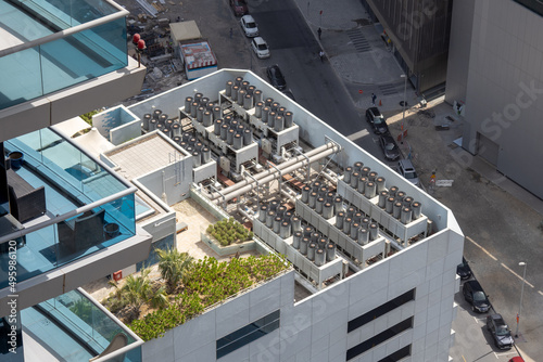 Mounted units of the air conditioning system on a modern skyscraper. A high-rise building with blue glass balconies and an industrial floor with cooling system evaporators and fan motors.