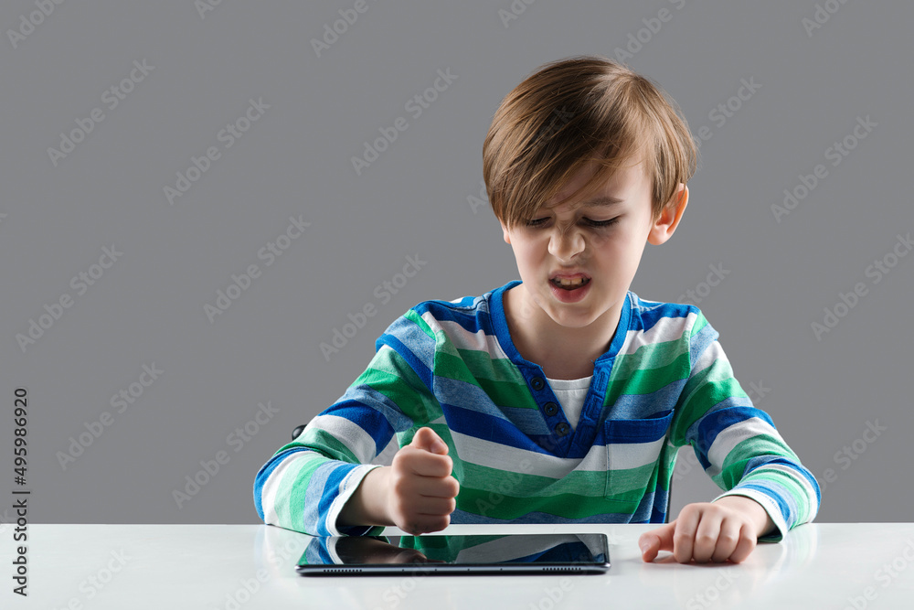 Angry boy hitting his tablet. Nervous boy studying online with laptop. Upset child has problem with gadget. Angry boy hitting his tablet. Nervous boy studying online with laptop. Upset child has problem with gadget.