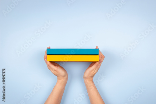 Female hands holding two blue and yellow color books over light blue background. Education, self-learning, book swap photo