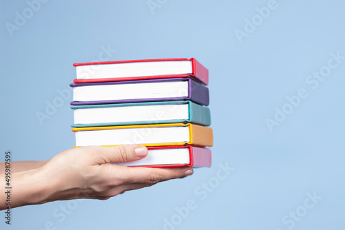 Female hands holding pile of books over light blue background. Education, self-learning, book swap, hobby, relax time