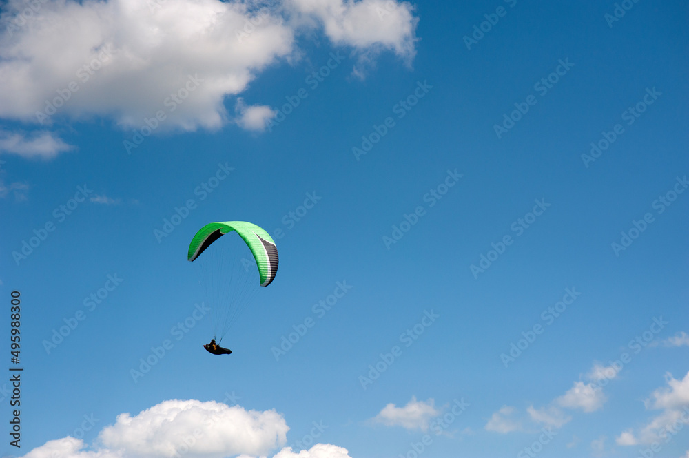 Alone green paraglider flying in the blue sky against the background of clouds. Paragliding in the sky on a sunny day. Alone green paraglider flying in the blue sky against the background of clouds. Paragliding in the sky on a sunny day.