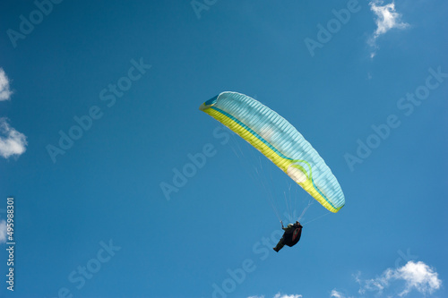 Alone blue and yellow paraglider flying in the blue sky against the background of clouds. Paragliding in the sky on a sunny day.