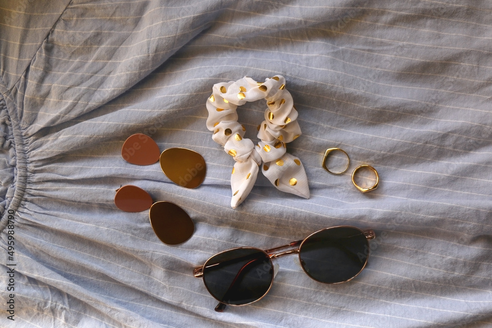 Blue linen shirt, sunglasses, white scrunchie, gold rings and fashionable earrings. Flat lay.